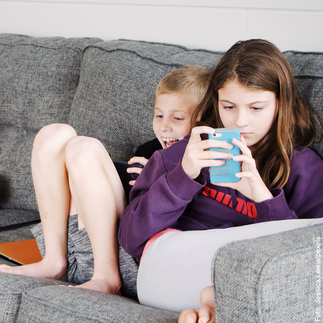 2 Schulkinder sitzen auf dem Sofa und spielen mit ihren Handys