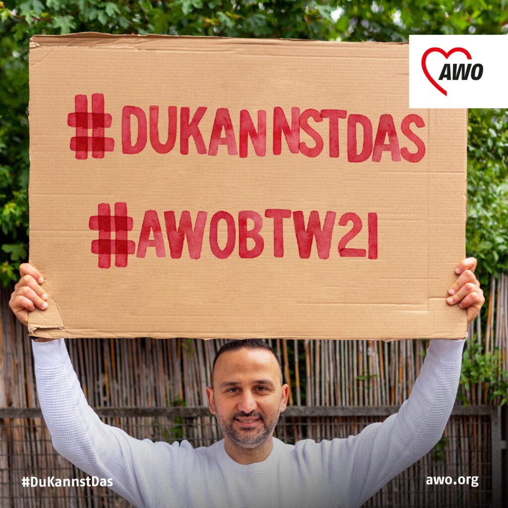 Ein Mann hält ein Plakat hoch mit den Hashtags #DuKannstDas und #AWOBTW21