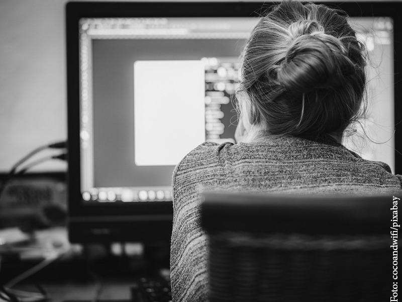 junge Frau schaut auf einen Monitor, von hinten fotografiert