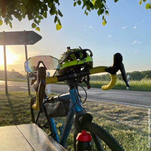 Fahrrad lehnt an einer Bank, im Hintergrund ein Sonnenuntergang