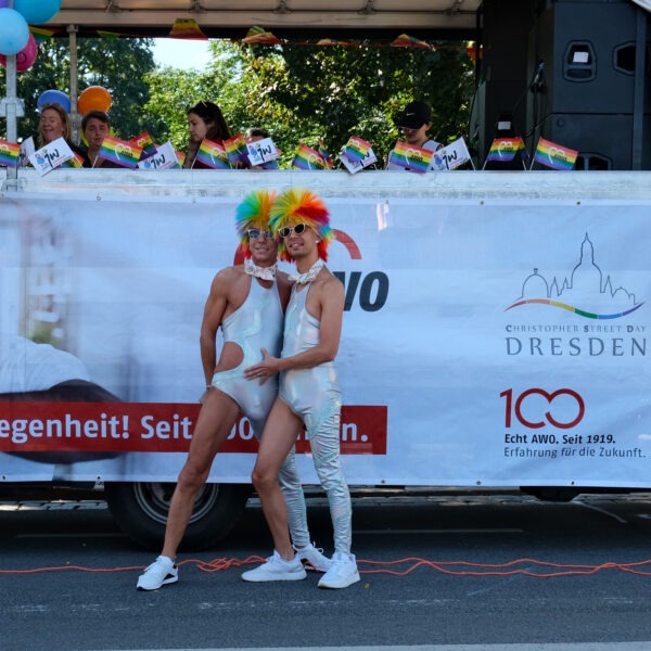 zwei gut gestylte queer Menschen mit bunten Haaren vor dem CSD Truck