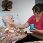 Eine Pflegerin reicht einer alten Frau einen Becher Tee