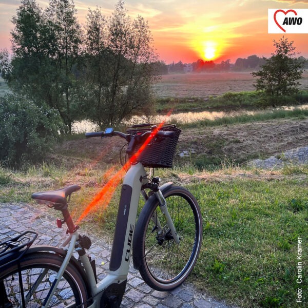 Ein Fahrrad vor einem kleinen Fluss, im Hintergrund geht die Sonne unter
