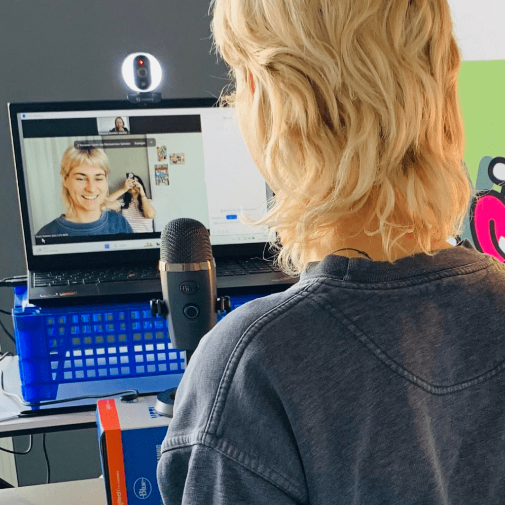 Eine Frau steht während eines Online-Workshops vor einem Mikrofon und einem Laptop