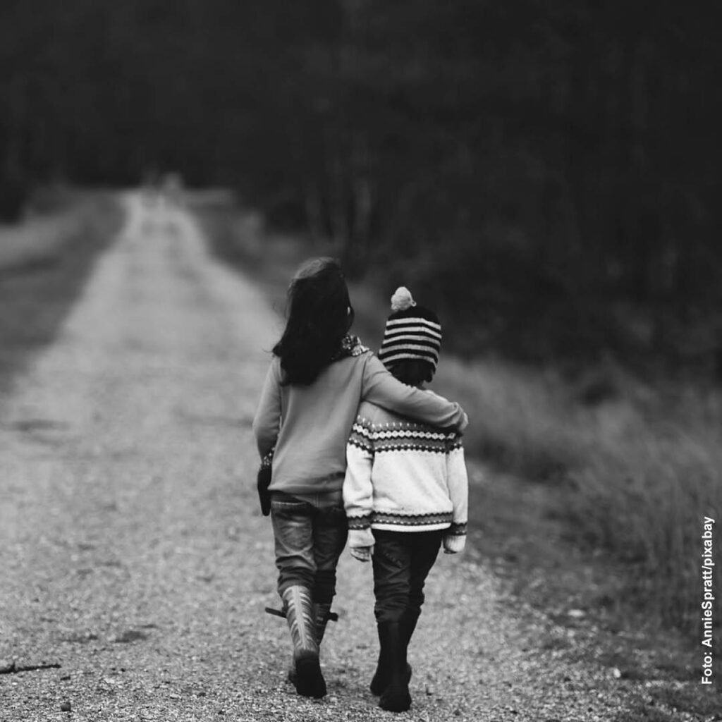 schwarz-weiß Bild zweier Kinder, die Arm in Arm einen Weg entlanglaufen