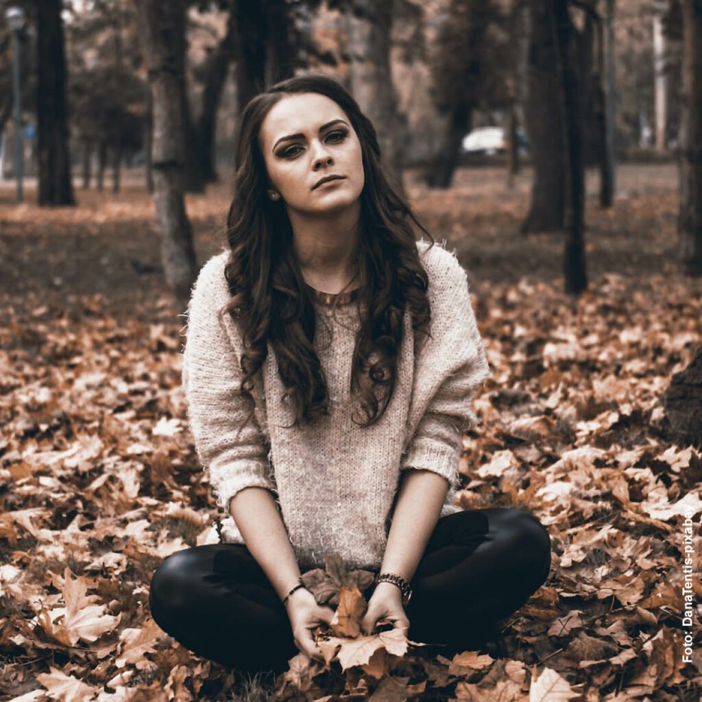 eine junge Frau sitzt im Schneidersitz in einem Park im Herbst