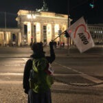 Eine Frau schwenkt die AWO Fahne vor dem beleuchteten Brandenburger Tor im Dunklen