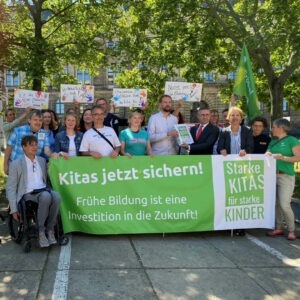 Die Bündnispartner:innen halten das Banner zur Kampagne hoch, Wilfried Kühner die Unterschriftenliste