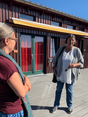 Kathrin Sonnenholzner steht im Austausch mit Daniela Jacobs, Teamleiterin der Freiwilligendienste, vor einem Holzgebäude mit roten Vorhängen. Beide unterhalten sich bei sonnigem Wetter auf einer Terrasse.