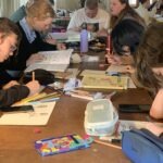 Jugendliche sitzen an einem Tisch und basteln gemeinsam während eines Seminars im Jugendfreiwilligendienst