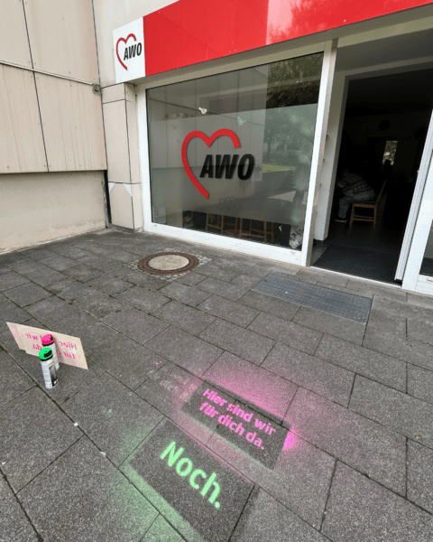 Eingang einer AWO-Einrichtung in Dresden-Prohlis mit der Kreidebotschaft ‚Hier sind wir für dich da. Noch.‘ auf dem Gehweg.“