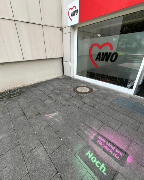 Eingang einer AWO-Einrichtung in Dresden-Prohlis mit der Kreidebotschaft ‚Hier sind wir für dich da. Noch.‘ auf dem Gehweg.“
