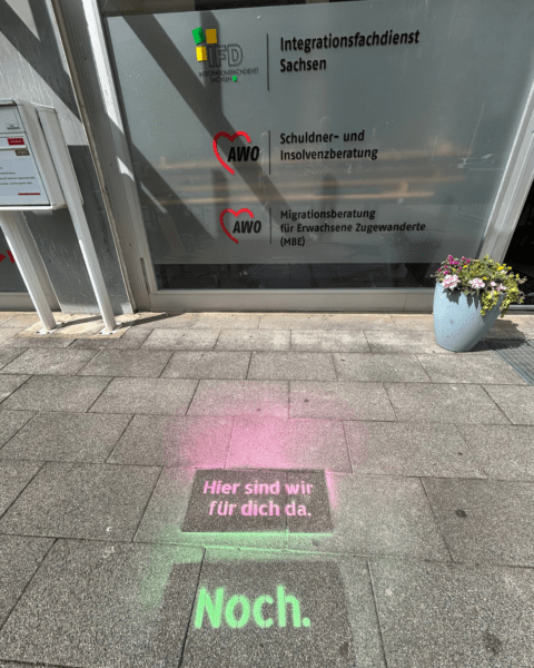 Eingang eines AWO-Beratungsstandorts in Dresden-Prohlis mit Hinweisen auf verschiedene Beratungsangebote und der Kreidebotschaft ‚Hier sind wir für dich da. Noch.‘ auf dem Boden.“