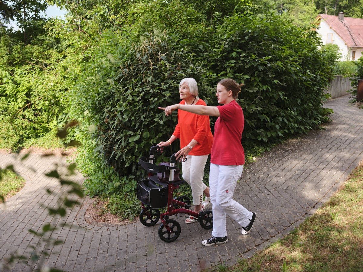 eine junge Frau geht mit einer älteren Frau im Rollator im Park spazieren